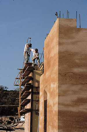 A prepared mixture of moistened soil and cement is shoveled into sturdy, two-sided, wooden forms set on a foundation, then compacted layer upon layer to form rock-hard, rammed-earth walls.